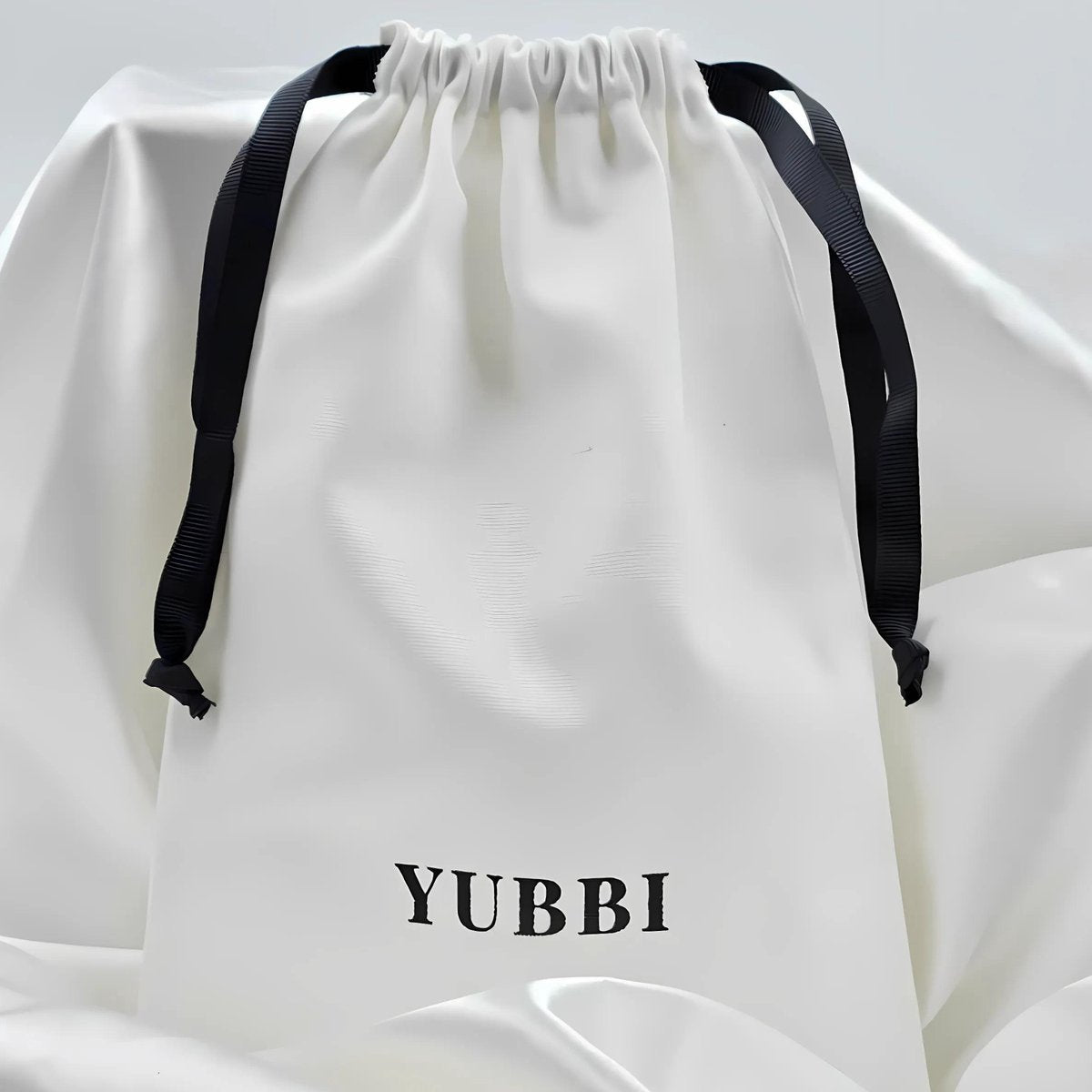 White drawstring bag with black straps and 'YUBBI' branding on a white background